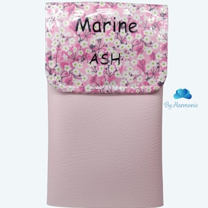 Puede incluir: Un estuche de cuero rosa claro con una solapa estampada floral. La solapa presenta un fondo rosa con flores blancas y las palabras "Marine ASH". La parte inferior del estuche es de color rosa claro liso. Las palabras "Rose clair" est&aacute;n en la parte inferior.