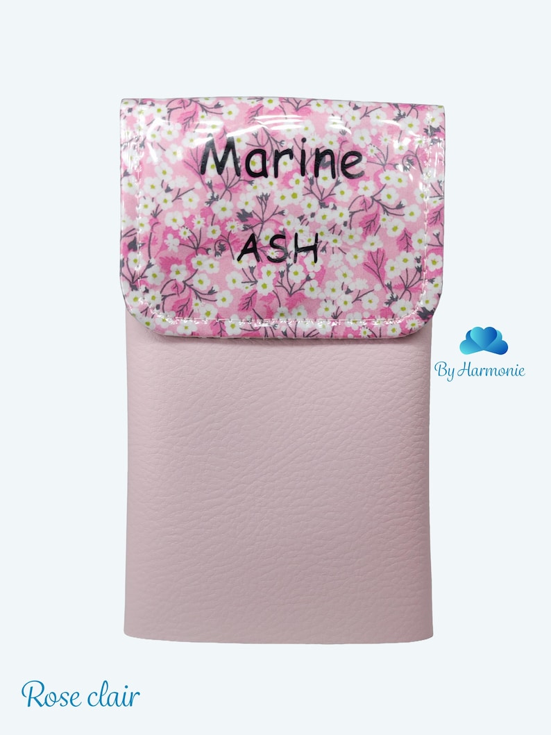 Puede incluir: Un estuche de cuero rosa claro con una solapa estampada floral. La solapa presenta un fondo rosa con flores blancas y las palabras "Marine ASH". La parte inferior del estuche es de color rosa claro liso. Las palabras "Rose clair" est&aacute;n en la parte inferior.
