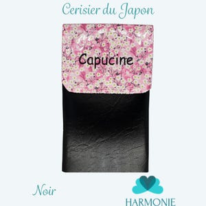 Puede incluir: Cartera negra con solapa con estampado floral rosa y la palabra "Capucine". La cartera tiene el texto "Pochette Cerisier du Japon" y "Harmonie By Sara Michel". Tambi&eacute;n es visible la palabra "Noir".