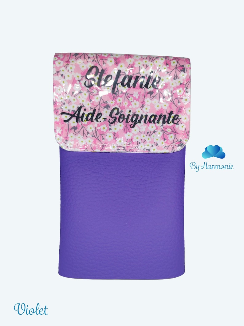 Puede incluir: Un estuche cil&iacute;ndrico violeta con una superficie texturizada. La solapa superior presenta un dise&ntilde;o floral rosa con el nombre "Stefanie" y las palabras "Aide-Soignante" en escritura negra. Un accesorio pr&aacute;ctico.
