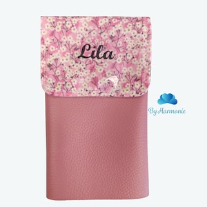 Puede incluir: Un estuche rosa con una solapa estampada con flores. La solapa presenta un dise&ntilde;o floral blanco y rosa con el nombre "Lila" en escritura negra. El cuerpo principal del estuche es rosa liso y texturizado.