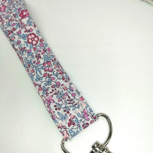 May include: A white fabric lanyard with a pink and blue floral pattern and a silver swivel clasp.