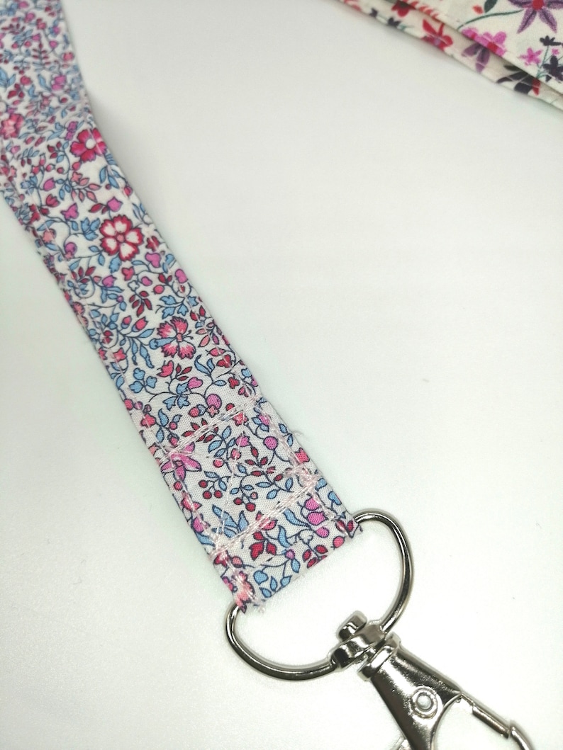 May include: A white fabric lanyard with a pink and blue floral pattern and a silver swivel clasp.