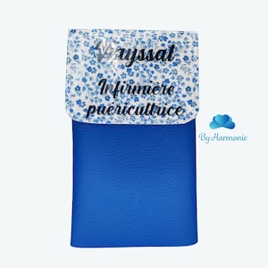 Peut inclure: Un portefeuille bleu avec un rabat à motifs floraux. Le rabat présente un fond blanc avec de petites fleurs bleues et le texte "Vayssat Infirmière puéricultrice" en écriture noire. Le portefeuille est de couleur bleu uni.