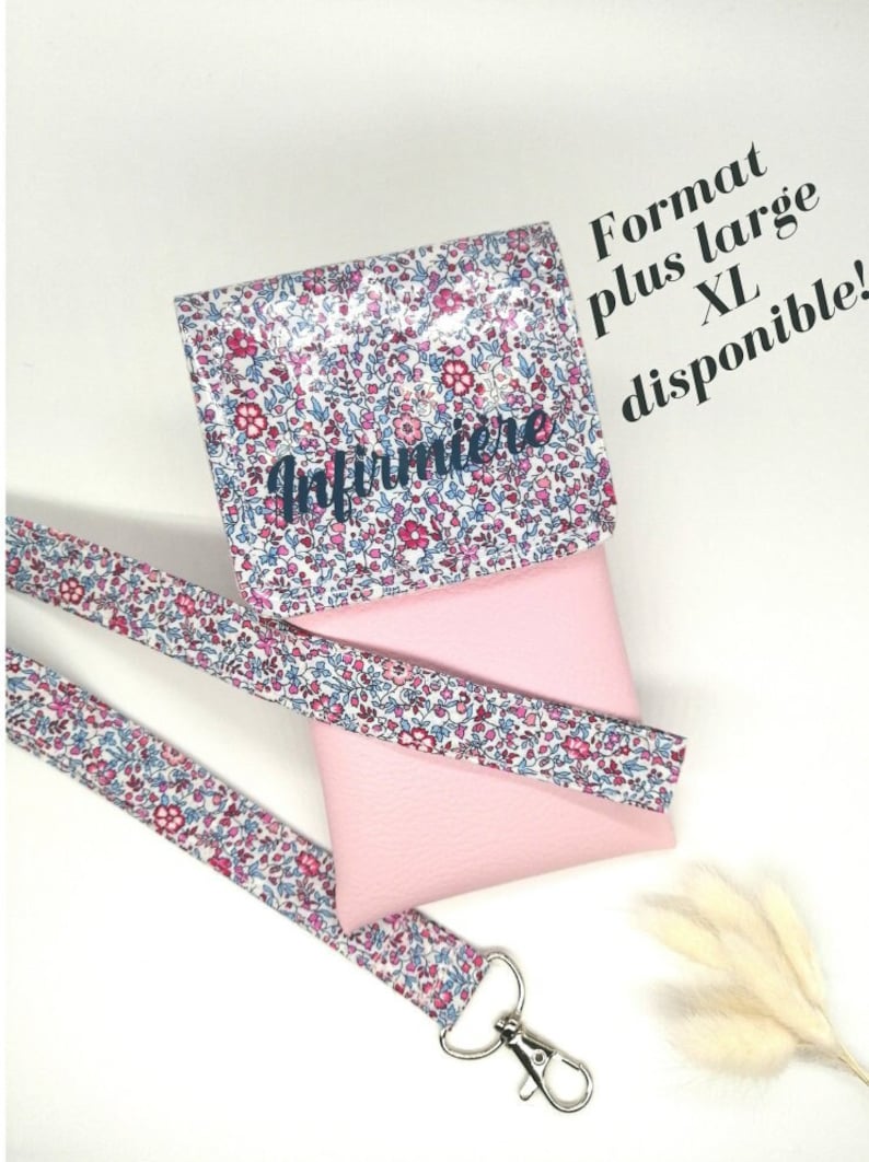 May include: A pink phone case with a floral pattern and a matching lanyard. The case has the word "Infirmiere" printed on it. The text "Format plus large XL disponible!" is written in black on a white background.