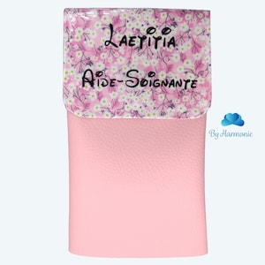 Puede incluir: Una cartera de polipiel rosa con solapa estampada floral. La solapa presenta el nombre "Laetitia" y el t&iacute;tulo "Aide-Soignante" en escritura negra. La palabra "Rose" est&aacute; escrita en cursiva en la parte inferior.