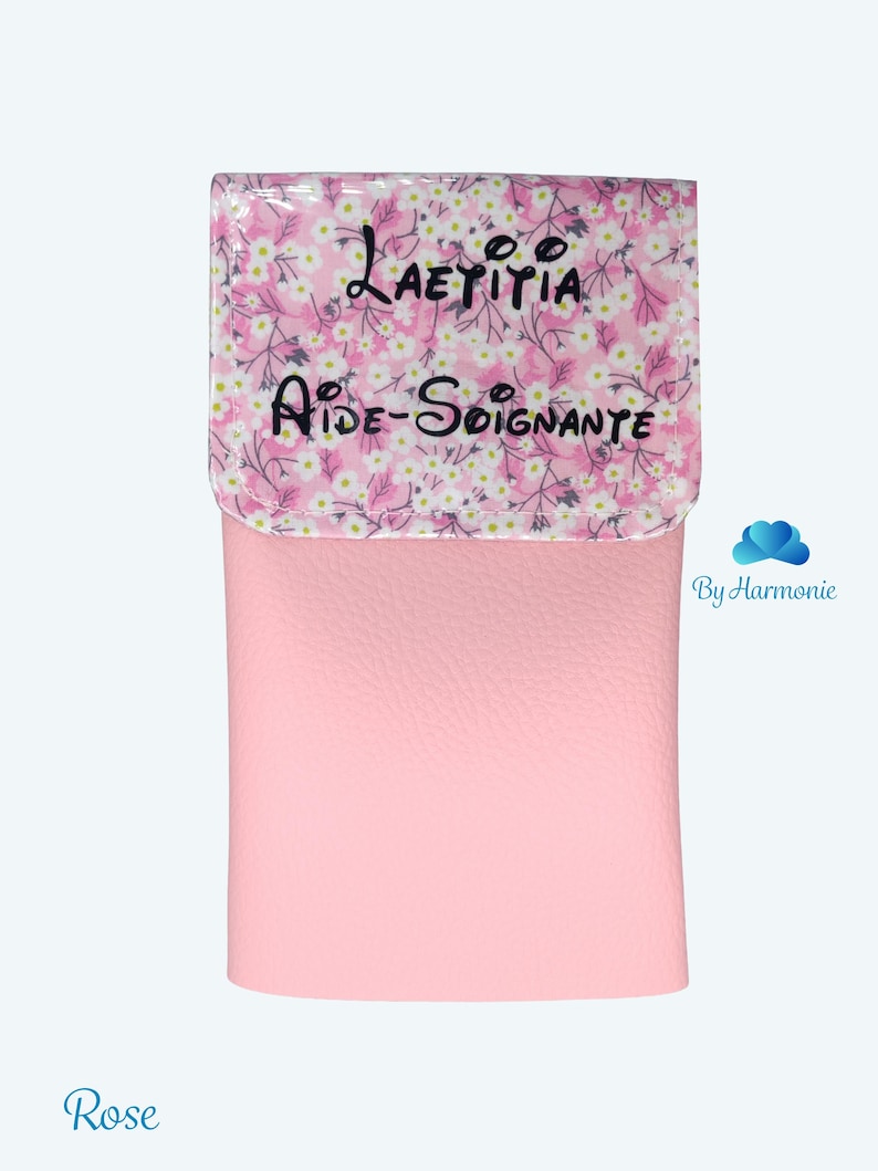 Puede incluir: Una cartera de polipiel rosa con solapa estampada floral. La solapa presenta el nombre "Laetitia" y el t&iacute;tulo "Aide-Soignante" en escritura negra. La palabra "Rose" est&aacute; escrita en cursiva en la parte inferior.