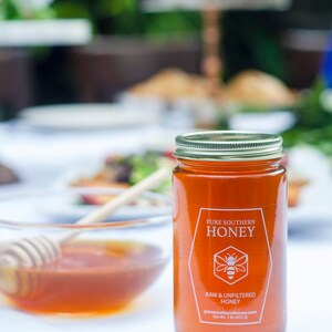 Puede incluir: Un tarro de vidrio de miel del sur puro con una etiqueta blanca que dice "Pure Southern Honey, Raw & Unfiltered Honey, puresouthernhoney.com, Net Wt. 1 lb. (453 g)".