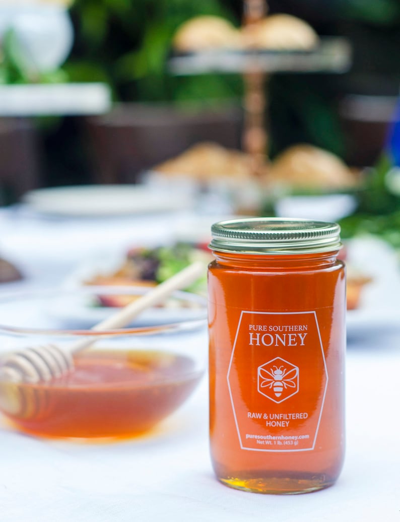Puede incluir: Un tarro de vidrio de miel del sur puro con una etiqueta blanca que dice "Pure Southern Honey, Raw & Unfiltered Honey, puresouthernhoney.com, Net Wt. 1 lb. (453 g)".