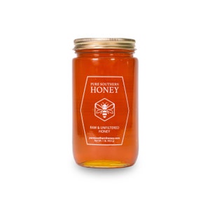 Puede incluir: Un tarro de vidrio de miel con una tapa dorada. La etiqueta dice "Pure Southern Honey" con una ilustraci&oacute;n de abeja y el texto "Miel cruda y sin filtrar" y "puresouthernhoney.com". El tarro contiene 1 libra (453 gramos) de miel.