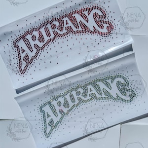May include: Two rectangular iron-on rhinestone transfers on white backing sheets. The top transfer features the word "AIRRANS" in red rhinestones, while the bottom transfer displays the same word in clear, iridescent rhinestones.