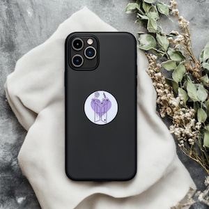 Puede incluir: Una funda de teléfono negra con una pegatina en forma de corazón morado con un diseño floral y un par de puertas abiertas.