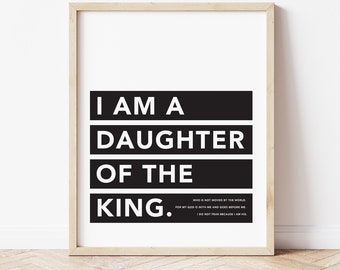 May include: A framed print with the text "I AM A DAUGHTER OF THE KING." The text is in bold white letters on black rectangular blocks. Additional text at the bottom reads "WHO IS NOT MOVED BY THE WORLD... I DO NOT FEAR BECAUSE I AM HIS."