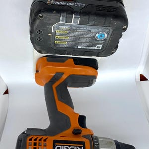 K&ouml;nnte beinhalten: Ein schwarzer und orangefarbener Ridgid-Bohrer mit einem 18-V-Lithium-Ionen-Akku. Der Bohrer hat eine Kupplungseinstellung von 1 bis 22. Der Akku tr&auml;gt den Text "RIDGID 18.0V LI-ION 2.71Ah".