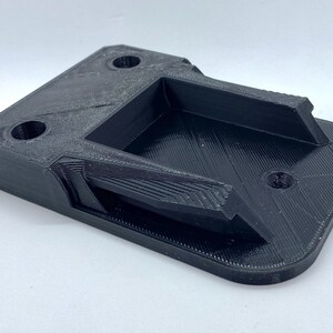 K&ouml;nnte beinhalten: Ein schwarzer 3D-gedruckter Kunststoffhalter mit einer rechteckigen &Ouml;ffnung und zwei runden L&ouml;chern.