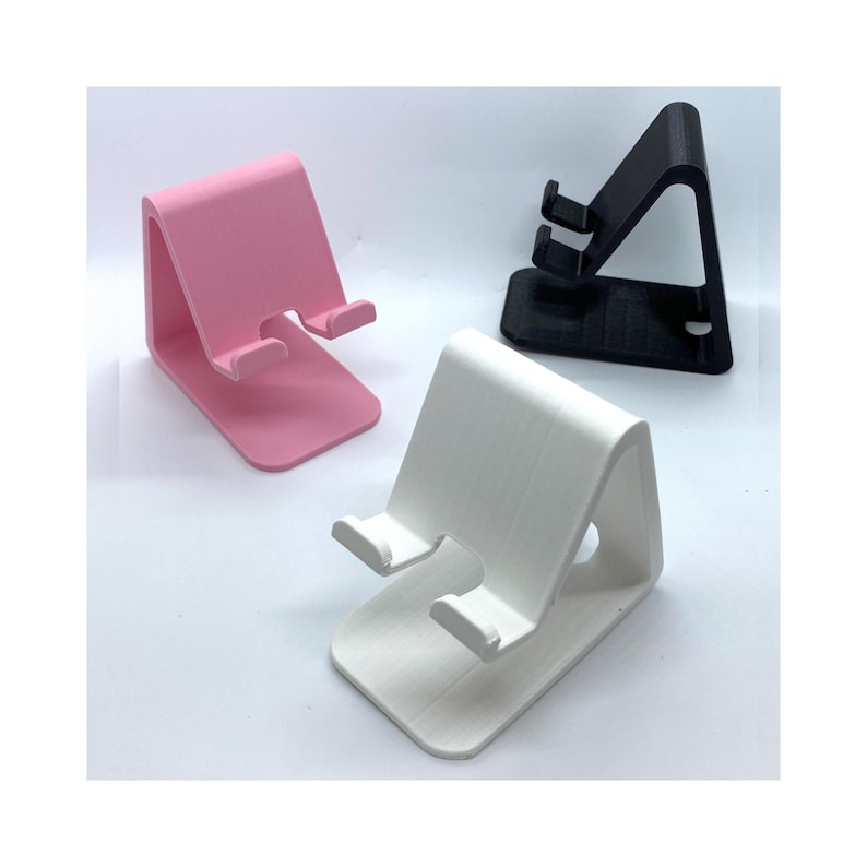 Peut inclure: Trois supports de t&eacute;l&eacute;phone de diff&eacute;rentes couleurs&nbsp;: rose, blanc et noir. Les supports sont en plastique et ont une forme triangulaire.