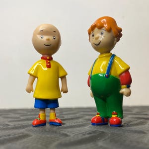 以下が含まれることがあります： プラスチック製のキャラクターフィギュア2体。1体目は髪がなく、黄色いシャツ、青いショートパンツ、赤と青の靴を着用。2体目はオレンジ色の髪で、黄色いシャツ、緑色のオーバーオール、赤い靴を着用している。