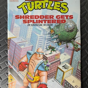 Puede incluir: Un cómic vintage de las Tortugas Ninja. La portada muestra un paisaje urbano con un helicóptero verde y el título "Shredder Gets Splintered: An Adventure to Color." También aparece un personaje grande en amarillo y azul.