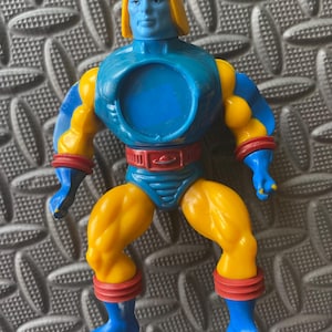 Puede incluir: Una figura de acción azul y amarilla con un casco rojo y amarillo. La figura tiene una abertura circular en el área del pecho.