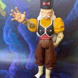 May include: A Dr. Gero action figure from Dragon Ball Z featuring a black hat with a red RR logo, white hair, a yellow shirt with puffed sleeves, a black vest, a red sash, and brown pants. The figure has a palm-out pose with a red sensor visible.