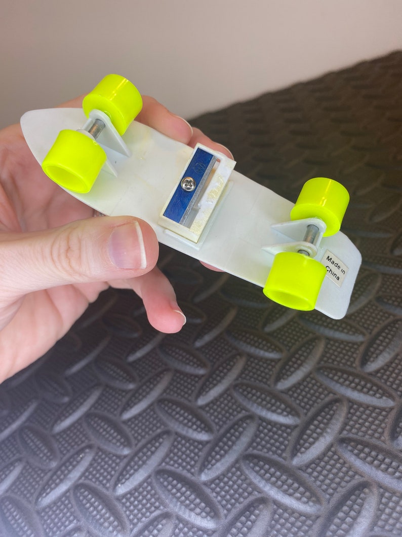 May include: A white skateboard pencil sharpener with yellow wheels. The sharpener has a blue blade and says "Made in China" on the bottom.