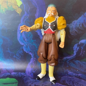 May include: An action figure of an elderly character with a white mustache, long white hair, and a blue head covering. The figure wears a yellow shirt with puffed sleeves, a black vest with red trim, brown pants, yellow leggings, and white shoes.