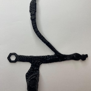 May include: Black, textured, decorative object with an abstract design. The object has a curved, elongated stem and a T-shaped base. The base features a hexagonal opening and a bulbous end with intricate detailing.