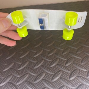 Puede incluir: Un sacapuntas de pl&aacute;stico blanco con forma de patineta con ruedas amarillas. El sacapuntas tiene una cuchilla azul y dice "Hecho en China" en el lateral.