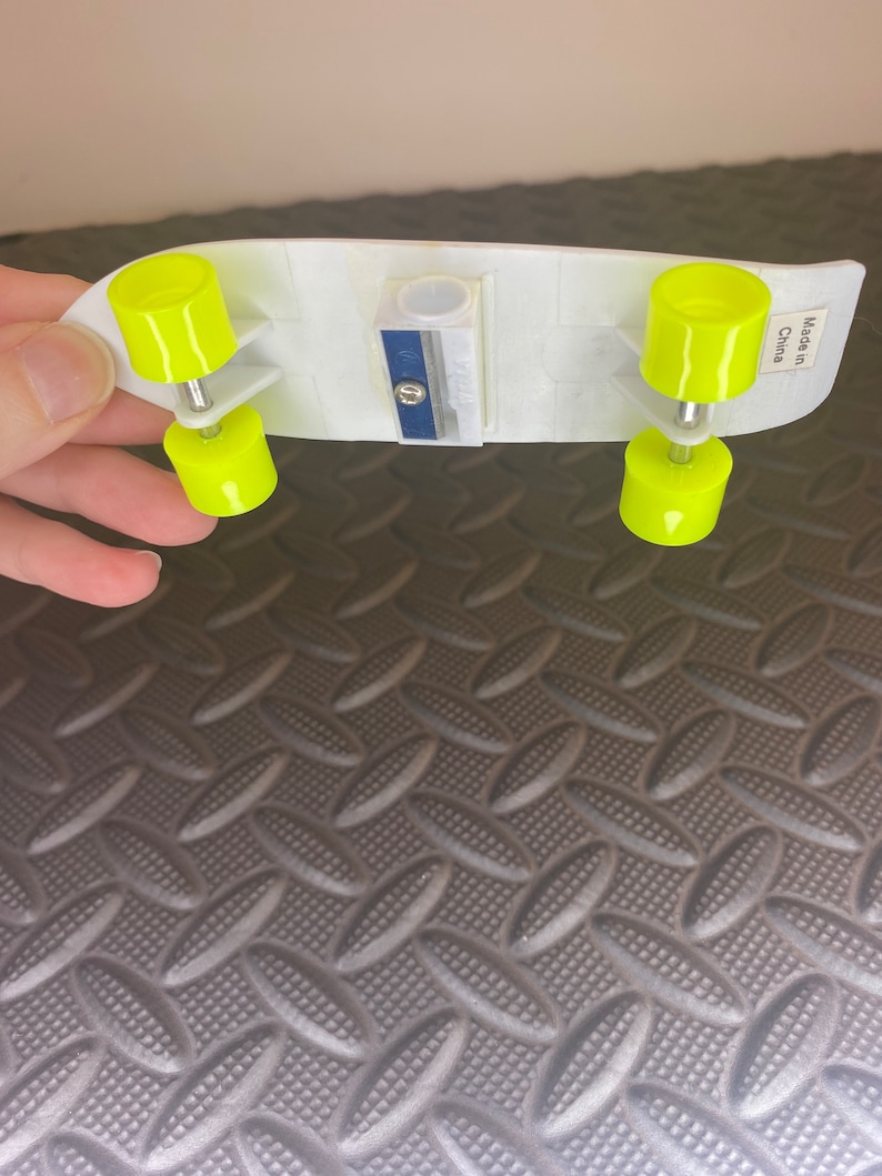 Puede incluir: Un sacapuntas de pl&aacute;stico blanco con forma de patineta con ruedas amarillas. El sacapuntas tiene una cuchilla azul y dice "Hecho en China" en el lateral.