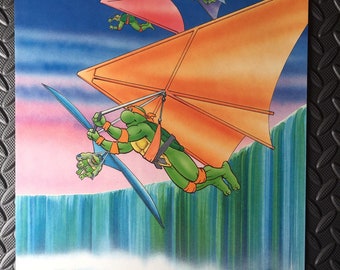 May include: A Teenage Mutant Ninja Turtles calendar featuring a colorful illustration of a turtle flying a hang glider over a waterfall. The calendar is for July and includes the days of the week and dates.