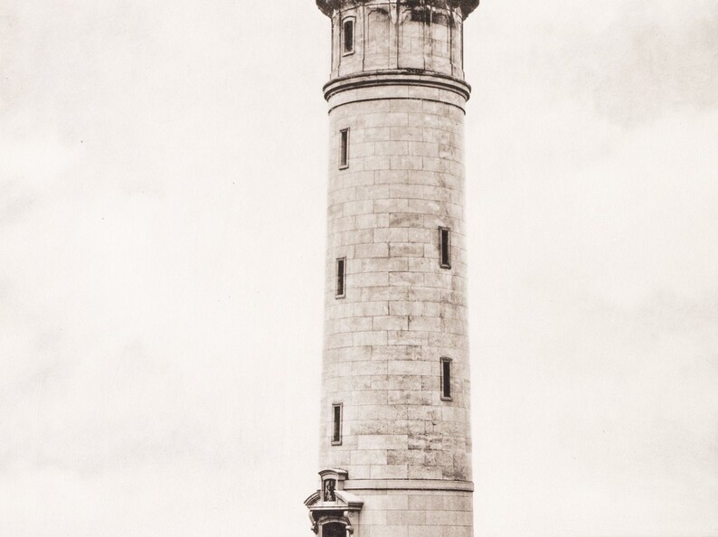 May include: A tall, white stone lighthouse with multiple windows. The lighthouse is against a cloudy sky.