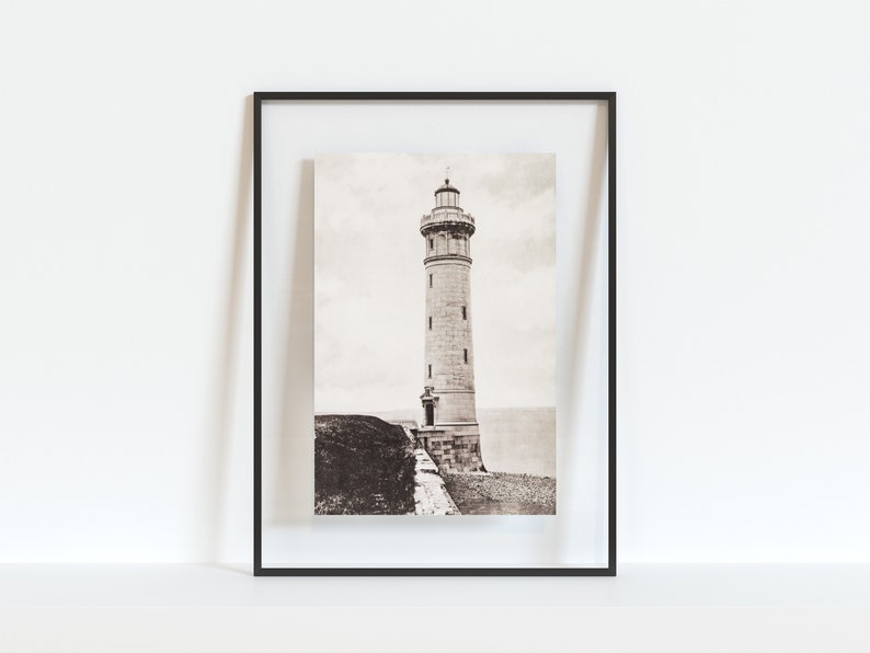 May include: A black and white photograph of a lighthouse on a cliff. The lighthouse is tall and has a white tower with a black roof. The photograph is framed in a black frame.