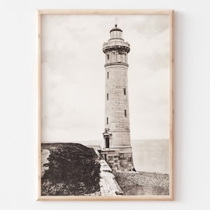 May include: A black and white photograph of a tall, stone lighthouse standing on a rocky shore. The lighthouse has a pointed roof and a small door at the base.