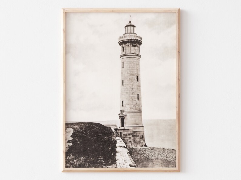 May include: A black and white photograph of a tall, stone lighthouse standing on a rocky shore. The lighthouse has a pointed roof and a small door at the base.