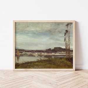 Pode incluir: Uma pintura de paisagem emoldurada retratando uma serena cena à beira-mar. A obra de arte apresenta um veleiro na água, edifícios ao longo da costa e um céu nublado. A pintura está em uma moldura de madeira clara, exibida contra uma parede branca.