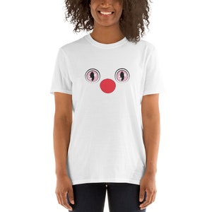 May include: White t-shirt with a cartoon face printed on the front. The face has two large pink eyes and a red nose.