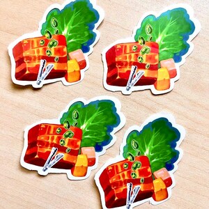 May include: Four stickers featuring a colorful illustration of a dish with red, orange, and green elements. Each sticker depicts a rectangular block of food, green leafy vegetables, and small orange cubes. Small silver tongs are also included in the design.