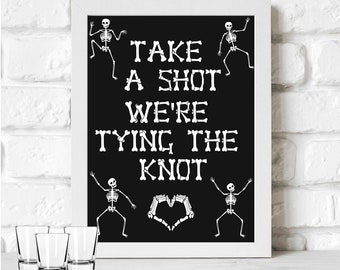 May include: A printable sign with a black background and white text that reads "Take a shot we're tying the knot". The text is made up of bones and there are four skeleton figures on the sign. There are four shot glasses in front of the sign.