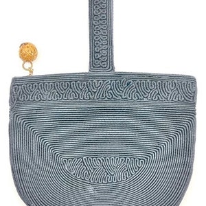 Op de afbeelding: Een grijze gehaakte handtas met een afgeronde bodem en een bovenste handvat. De tas heeft een decoratief patroon en een kleine houten kraal die aan het handvat is bevestigd.