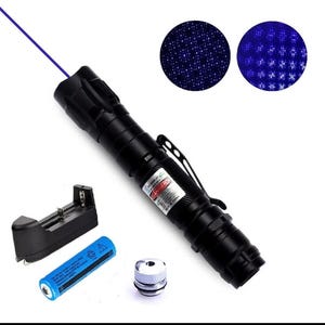May include: Black laser pointer with a blue beam, a charging base, a blue battery, and a silver and white attachment. Two circular images show the laser's light patterns. The laser has a pocket clip and a warning label.