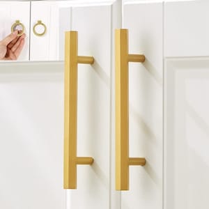 May include: Two gold cabinet pulls with a rectangular shape and a straight bar design. The pulls are mounted on a white cabinet door.