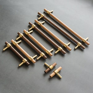 以下が含まれることがあります： 真鍮のアクセントが付いた木製のキャビネットプル12個セット。プルは明るい茶色と暗い茶色の2種類のウッドトーンで仕上げられています。プルは灰色の表面に三角形のパターンで配置されています。