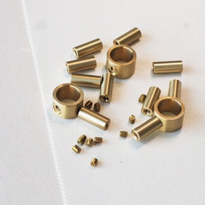 Pode incluir: Um conjunto de ferragens de latão para a fabricação de móveis, incluindo dois anéis, um conector de três vias e vários parafusos pequenos.
