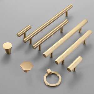 May include: Assortment of gold-toned cabinet hardware, including pulls, knobs, and a ring pull. The hardware is made of metal and has a polished finish.