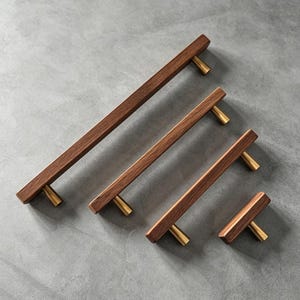 May include: Four cabinet pulls of varying lengths, each featuring a rectangular dark brown wood handle attached to two conical brass-colored metal posts. The pulls are arranged diagonally from longest to shortest, showcasing a consistent design.
