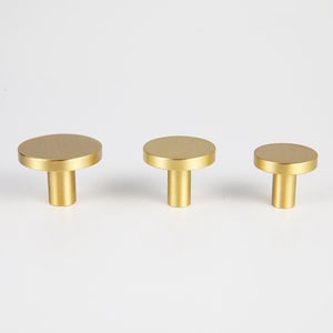 May include: Three gold-toned round cabinet knobs with a flat top and a cylindrical base.