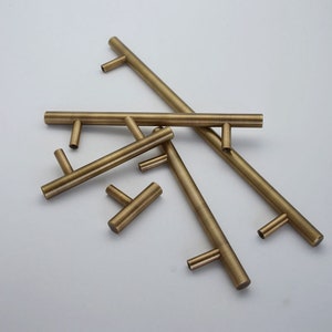 Pode incluir: Um conjunto de cinco puxadores de armário dourados com um design simples e moderno. Os puxadores são feitos de metal e têm um acabamento escovado.