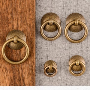 May include: Five antique brass cabinet door pulls with a decorative, fluted design. The pulls have a circular ring shape and are various sizes.