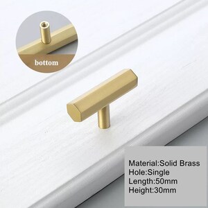 Pu&ograve; includere: Pomo per cassetti a forma di T dorato con base esagonale. Il pomo misura 50 mm di lunghezza e 30 mm di altezza. Materiale: Ottone massiccio. Foro: Singolo.