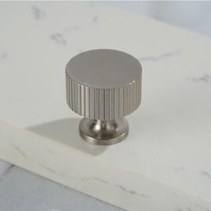 May include: A silver cabinet knob with a fluted design. The knob has a round top and a cylindrical base.